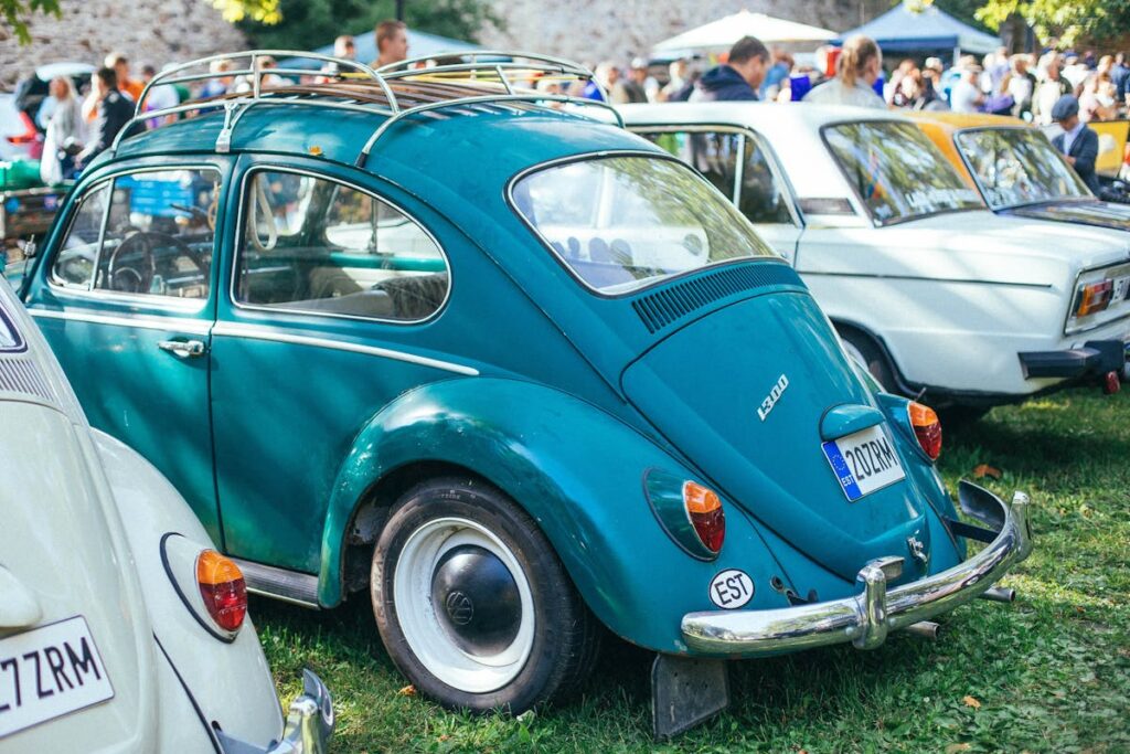 A teal Volkswagen Beetle displayed outdoors at a lively classic car show.