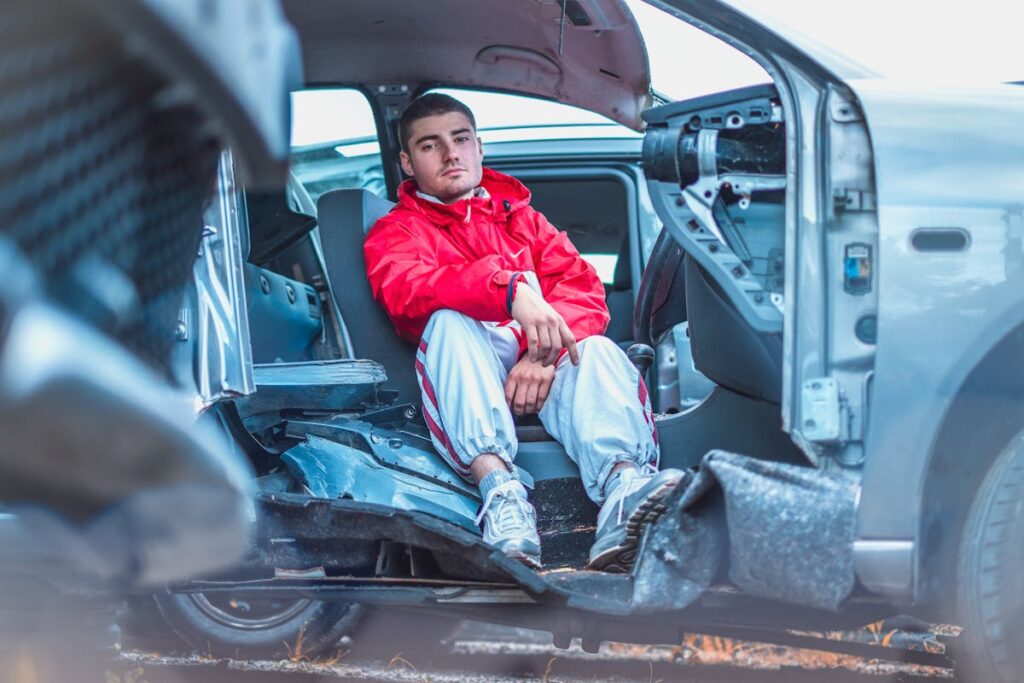 Man in Red Coat Sitting on Broken Car Seat