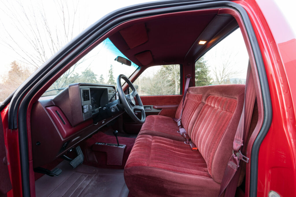 Portland, OR, USA – Dec 9, 2020 – 1990 Chevrolet Silverado 1500 regular cab interior with burgundy cloth bench seat, seat belts, manual gear shift, and classic vintage pickup truck cabin