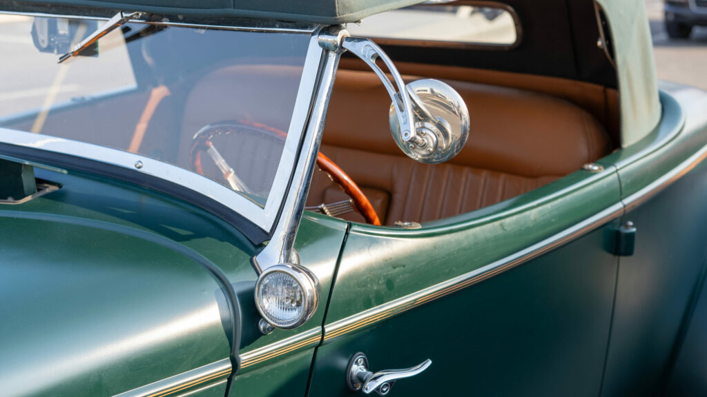 Close up of a classic green vintage convertible car featuring polished chrome details, a leather interior, curved windshield and elegant retro styling.