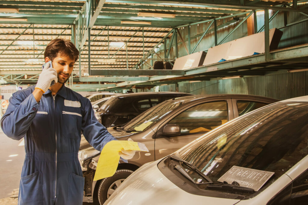 Male worker, auto mechanic, painter at accident damage collision checking history report repair list repainting car and cost to customer for insured car in comprehensive garage.